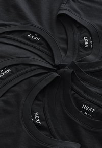 Magliette di cotone nero disposte in cerchio, con scollature rotonde e etichette di marca visibili con la scritta "NEXT M".