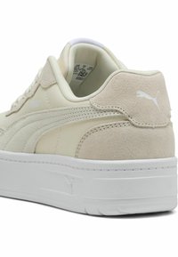Les baskets Puma présentent un dessus en cuir crème avec des accents en daim beige, une semelle en caoutchouc blanche et un design classique avec une silhouette basse.