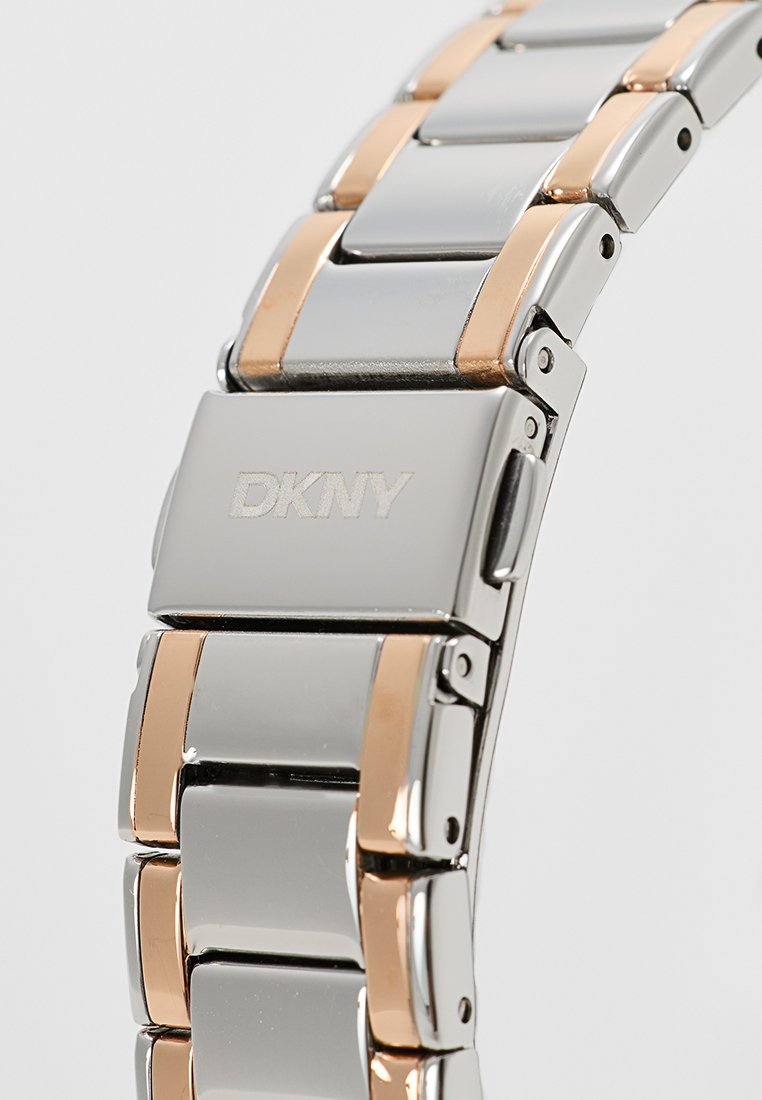 Zegarek DKNY z srebrno-różowym stalowym paskiem ze prostokątnymi ogniwami i polerowanym wykończeniem. Zapięcie na zatrzask na pasku.