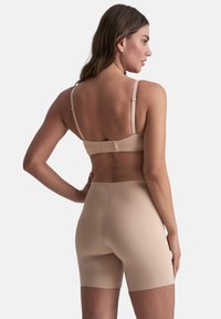 Beige bh met verstelbare schouderbanden en haaksluiting, gecombineerd met bijpassende shapewear-shorts. Glad, rekbaar materiaal met een naadloos ontwerp.