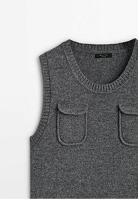 Pull sans manches gris tricoté avec deux petites poches à rabat à l'avant et un col rond côtelé.