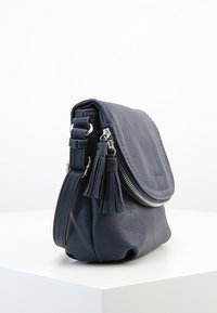 Mørkeblå læder crossbody taske med klap, sølv lynlås, kvastdetaljer og justerbar strop på en hvid overflade, set fra siden.