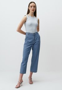 Top in maglina azzurro chiaro con dettagli sulle spalle a taglio, abbinato a jeans azzurri chiari a vita alta e ghette con tacco argento.