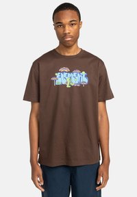 Bruine katoenen t-shirt met kleurrijk grafisch ontwerp met het woord "ELEMENT" en paddenstoelenmotieven op de voorkant. Korte mouwen, ontspannen pasvorm.