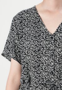 Vestido preto com um padrão floral branco, apresentando um decote em V, mangas curtas e botões ao longo da frente, feito de um tecido leve.