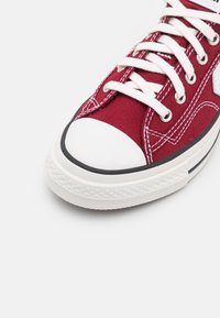 Rote Leinensneaker mit weißer Gummikappe und Sohle. Verfügt über weiße Schnürsenkel, silberne Ösen und kontrastierende Nähte.