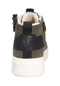 Stivale ankle in suede verde oliva con dettagli in pelle nera, suola in gomma bianca e chiusura con zip. Presenta una fodera in pelliccia e un dettaglio distintivo.