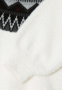 Vit fleece-tyg med en mjuk textur, med en svart och grå mönstrad stickad halsringning med diamantmotiv och subtila glittriga inslag.