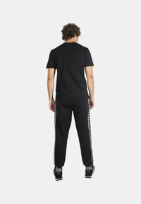T-shirt nera e pantaloni jogger neri con strisce bianche laterali, caratterizzati da una vestibilità regolare e da una texture liscia simile al cotone, abbinati a sneakers nere.