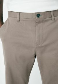 Light brown chinos made of cotton, featuring a straight cut, subtle texture, front pockets, and a single black button closure.