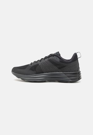 Chaussures de sport noires avec tige en mesh et synthétique, bout rond, surface texturée, et une semelle épaisse ondulée pour un amorti supplémentaire.