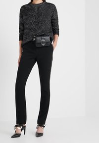 Svart stickad tröja med mönstrad textur, kombinerad med svarta tajta byxor med sidostuds och svarta spetsiga klackskor med ankelband.