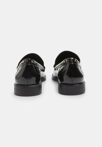 Pantofi negri din piele lacuită, cu vârful rotunjit și toc mic, prevăzuți cu o curea decorativă cu capse argintii pe spate.