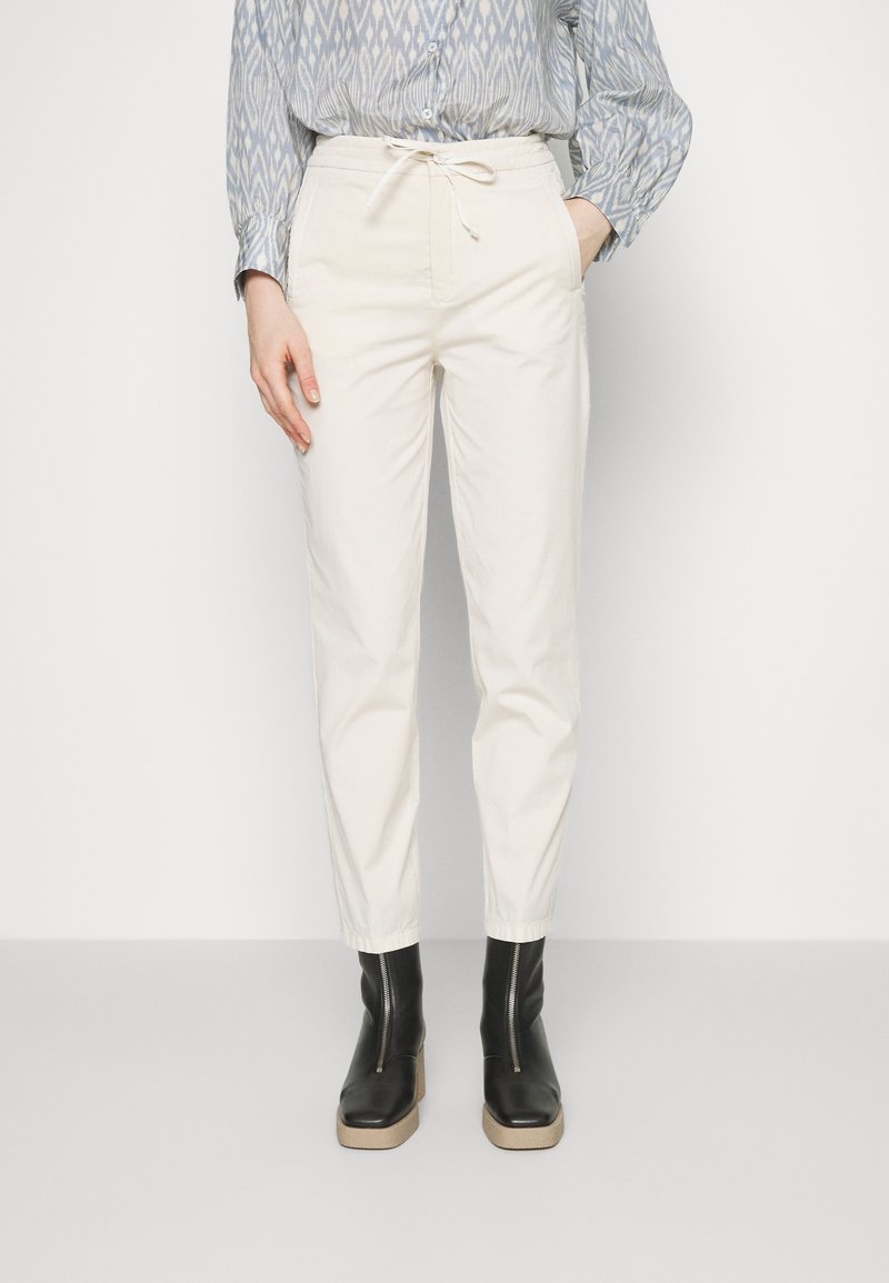 Beige, schmal zulaufende Hosen aus Baumwolle mit einem elastischen Bund und Kordelzug, kombiniert mit schwarzen Stiefeletten mit einer klobigen Sohle.