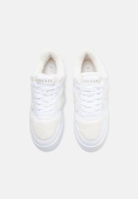 Baskets blanches avec une texture douce et pelucheuse sur les côtés, un laçage et un marquage "GUESS" sur la languette. Semelle plate.