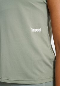 Ljusgrönt ärmlöst sportlinne av texturerat tyg med en vit logotyp på sidan. Designen är minimalistisk med en slät yta.