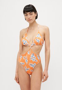 Fato de banho inteiro em laranja com padrões florais azuis, com decote halter, copas triangulares, detalhes com recortes e pernas altas.