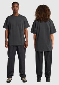 Mörkgrå oversized t-shirt med rund halsringning, i bomull. Bärs med vida svarta byxor med ett synligt nummer "223" på benet.