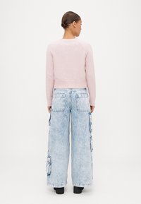 Jasnoróżowy krótki sweter z prążkowanym pasem, połączony z jasnoniebieskimi, dużymi spodniami cargo z denimu, posiadającymi boczne kieszenie i luźny krój.