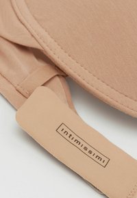 Beige bh med en jämn yta, som har en tagg med varumärket "Intimissimi" och en mjuk, justerbar rem.