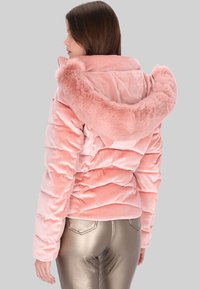 Růžová sametová prošívaná bunda s kapucí z umělé kožešiny, zdobená prošitým vzorem a žebrovanou texturou. Doplněno kovovými, přiléhavými kalhotami.