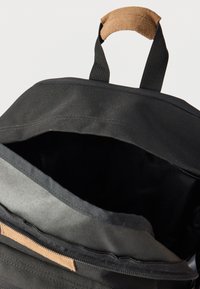 Μαύρο και γκρι σακίδιο ανοιχτό, που δείχνει άδειο το κύριο διαμέρισμα, με επενδυμένη καφέ λαβή σε λευκό φόντο.