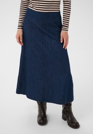Femme portant une jupe trapèze en denim bleu foncé, des bottes en cuir marron mi-mollet, et un haut à manches longues rayé marron et blanc.