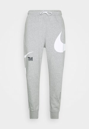 Vaaleanharmaat collegehousut, joissa valkoiset Nike-swoosh-logot jaloissa, joustavat resorit ja valkoinen kiristysnauha vyötäröllä.