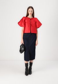 Top corto in satin rosso con maniche a sbuffo e nodo frontale. Abbinato a una gonna a tubino in denim scuro e stivali neri a punta. Borsa nera.