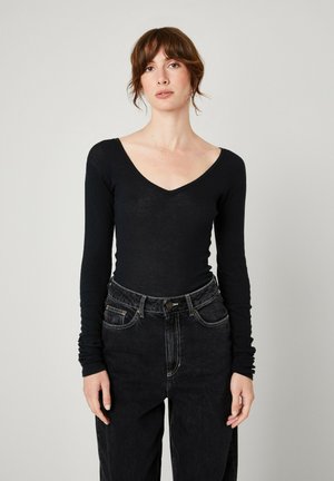 Black long-sleeve top with a V-neck, made of a lightweight material; paired with high-waisted dark denim jeans. Smooth texture, fitted design.