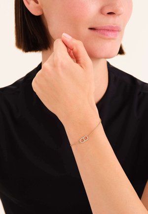 Pulsera de oro con una cadena delicada y un centro rectangular adornado con pequeñas piedras claras, usada en una muñeca.