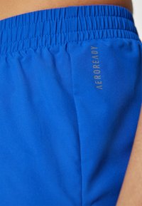 Pantalones cortos deportivos de color azul real con cintura elástica y logo AEROREADY en gris claro en el lateral. Textura suave, tejido ligero.