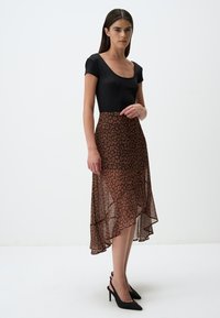 Bodysuit noir à côtes associé à une jupe en tulle transparente imprimée léopard marron avec un ourlet asymétrique. Porté avec des chaussures à talons hauts noires.
