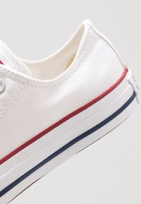 Baskets en toile blanche à profil bas, avec une semelle en caoutchouc rayée rouge et bleue et des œillets ronds en métal pour les lacets.