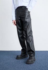 Svart faux skinnbukser med rett ben-design, glatt tekstur, sidelommer og kombinert med chunky svarte sko.