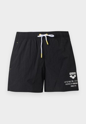 Μαύρο μαγιό σορτς με λευκό κορδόνι και κίτρινα άκρα, με λευκό λογότυπο και κείμενο στο δεξί πόδι.