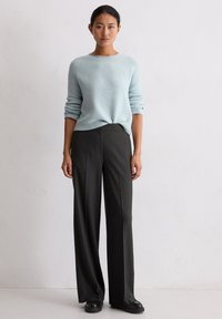 Jasnoniebieski sweter dziergany o prążkowanej strukturze i luźnym kroju, zestawiony z ciemnoszarymi spodniami w paski o szerokich nogawkach i czarnymi butami.