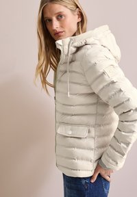 Ljusbeige puffjacka med huva, med horisontellt sydda sömmar, dragkedja framtill och ficka med tryckknapp. Texturerad krage som accent.