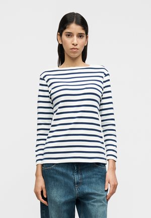 Tričko s dlhým rukávom v bielej farbe s námorníckymi pruhmi, s lodičkovým výstrihom a rovnakým strihom. Kombinované s voľnými modrými rifľovými nohavicami.