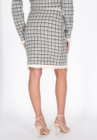 Fekete-fehér tweed szoknya bojtós szegéllyel, testhez simuló sziluett, kölcsönözve mezítláb pántos magassarkú szandálokkal. Strukturált szövetmintázat.