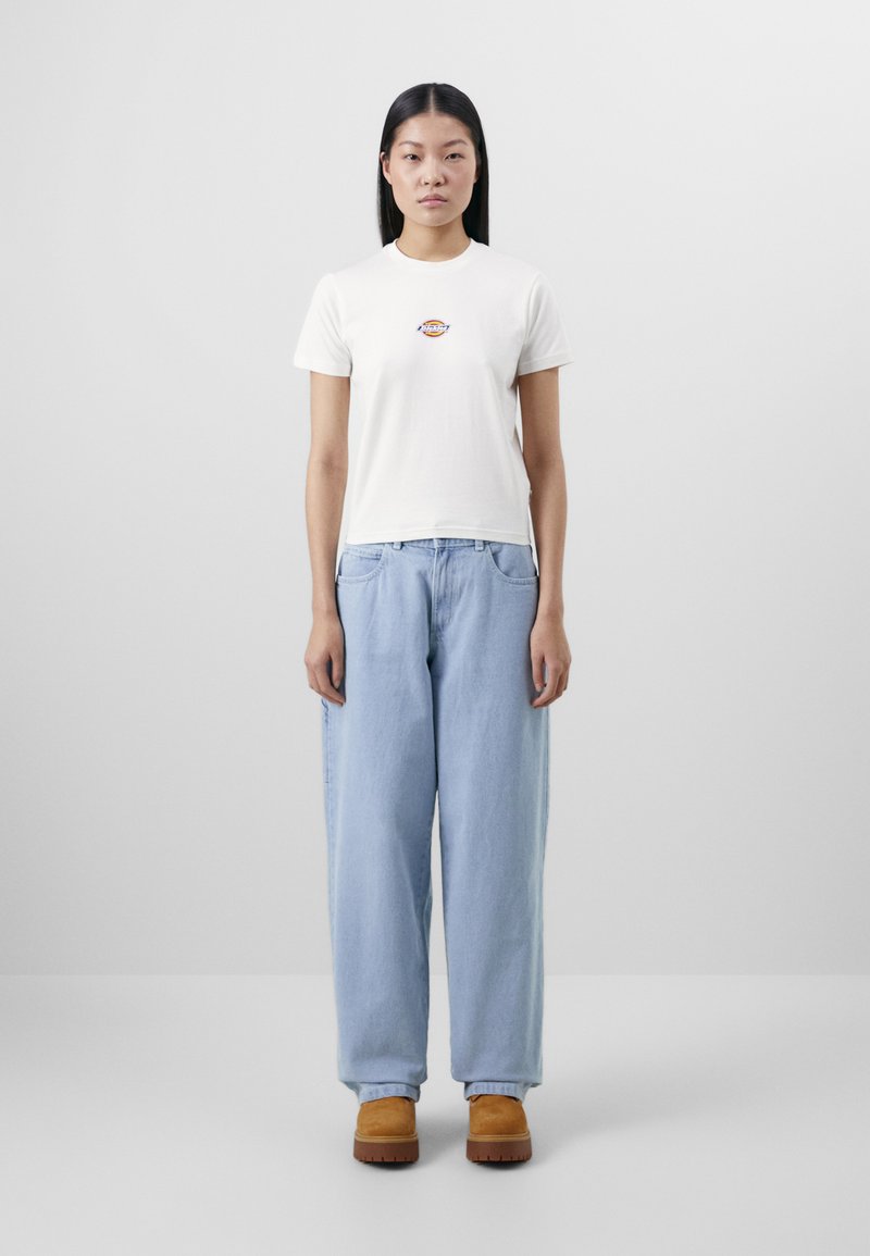 Hvit bomull t-skjorte med rund hals og liten grafisk detalj på brystet, sammen med lyseblå, løstsittende jeans og brune tresko.