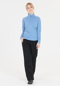 Hellesblaues Langarmoberteil mit Viertelreißverschluss, kombiniert mit schwarzen wasserdichten Hosen. Das Oberteil hat eine glatte Textur und eine enganliegende Passform, während die Hosen Taschen haben.