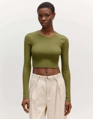 Olijfgroen lange mouw cropped top met een ribbelstructuur, gecombineerd met hoog opgesneden beige broek met zilveren hardwaredetails.