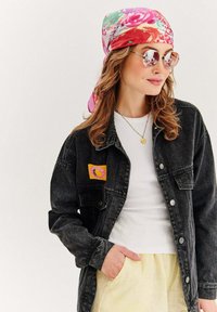 Czarna dżinsowa kurtka z żółtą i różową łatą, w zestawieniu z białą koszulą i jasnob żółtą spódnicą. Dodatki to różowy kwiatowy szalik i okrągłe okulary przeciwsłoneczne.