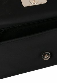 Bolso de nylon negro con herrajes dorados. Presenta una forma rectangular, cierre con cremallera y un acento de botón a presión. Textura suave.