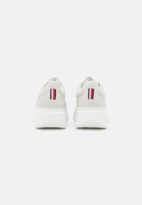Sneakers grigi chiari con un design elegante, caratterizzati da una suola bianca e un distintivo accento rosso, bianco e blu sul tallone.