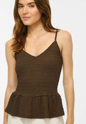 Femme portant un haut marron texturé sans manches avec de fines bretelles et un ourlet volanté, debout devant un fond blanc uni.