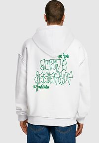 Weißer übergroßer Hoodie mit grüner Grafik auf dem Rücken, auf dem steht: "DIESE LIEBESGOTT ASSISTENTIN IST DEINER REIHE." Weicher Stoff, mit Kapuze.