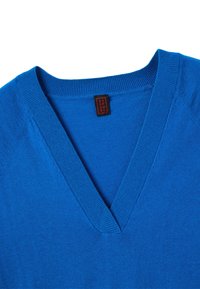 Pull bleu en V avec un col côtelé et une étiquette de vêtement rouge et noir à l'intérieur du col.