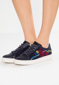 Navy leather sneakers with suede accents, featuring colorful embroidered floral designs and round white rubber soles.